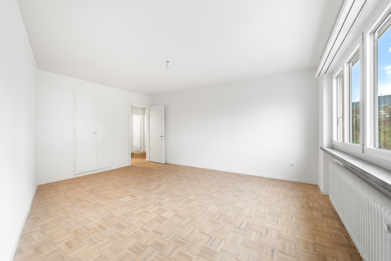 Helles, leeres Zimmer mit Parkettboden und Fensterfront