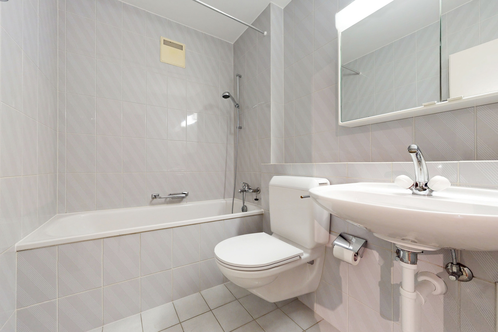 Kleines weiß gefliestes Badezimmer mit Badewanne, WC und Waschbecken