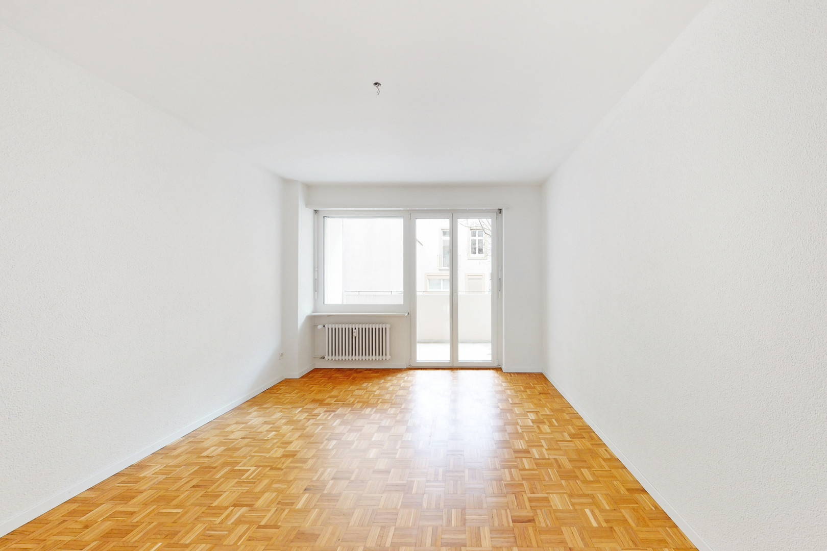 Leerer Wohnraum mit Balkon und Parkettboden