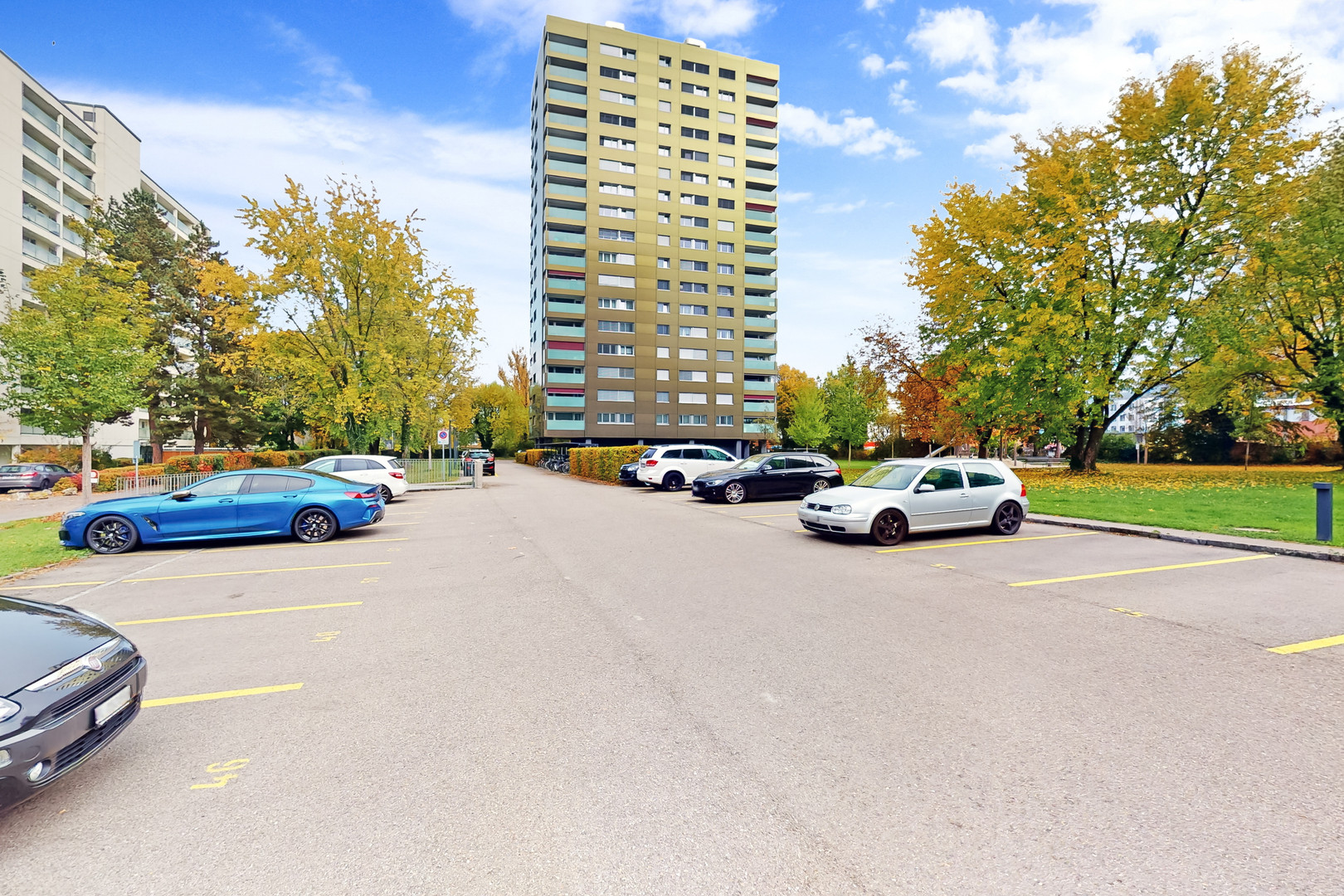 Wohnhochhaus mit Parkplatz und Herbstbäumen