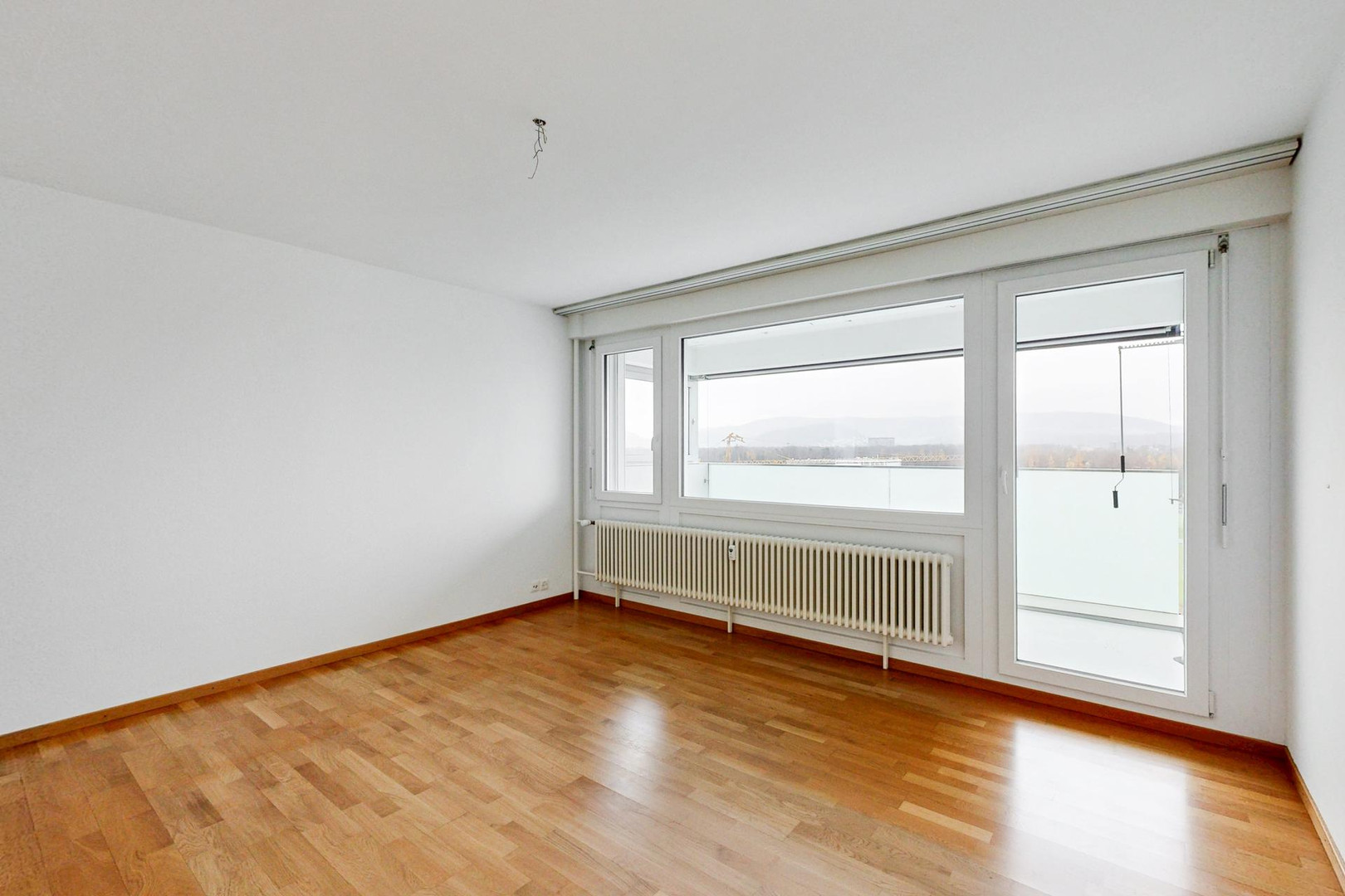 Heller leerer Wohnraum mit Balkon und großen Fenstern