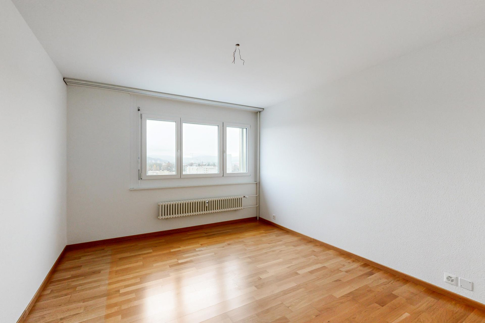 Leerer heller Raum mit Parkettboden und Fenster