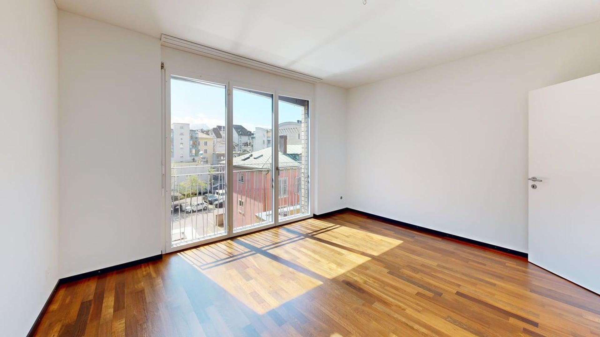 Helles leeres Zimmer mit Balkonfenster und Holzparkett