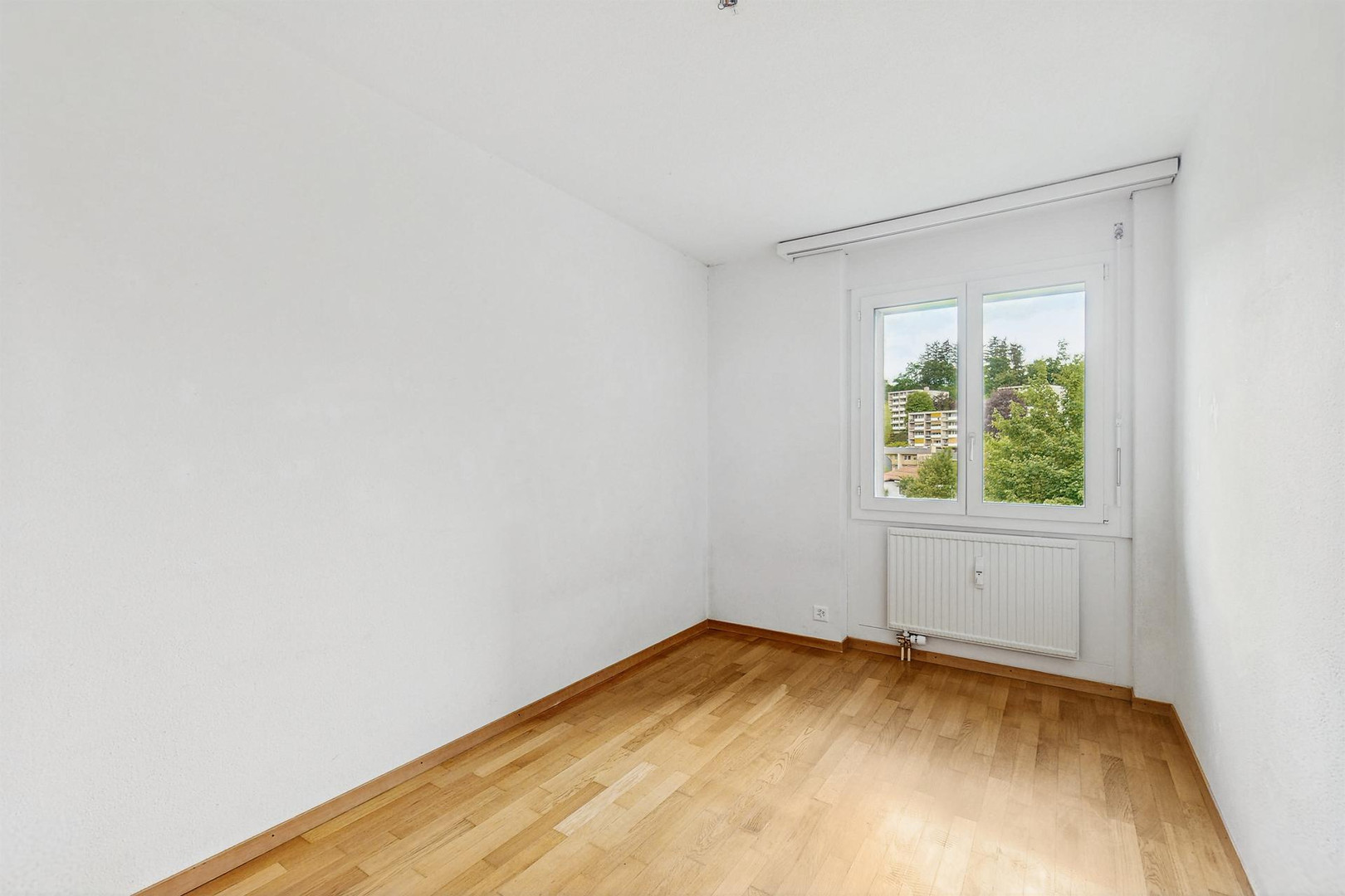 Helles, leeres Zimmer mit Holzfußboden und Fensterblick