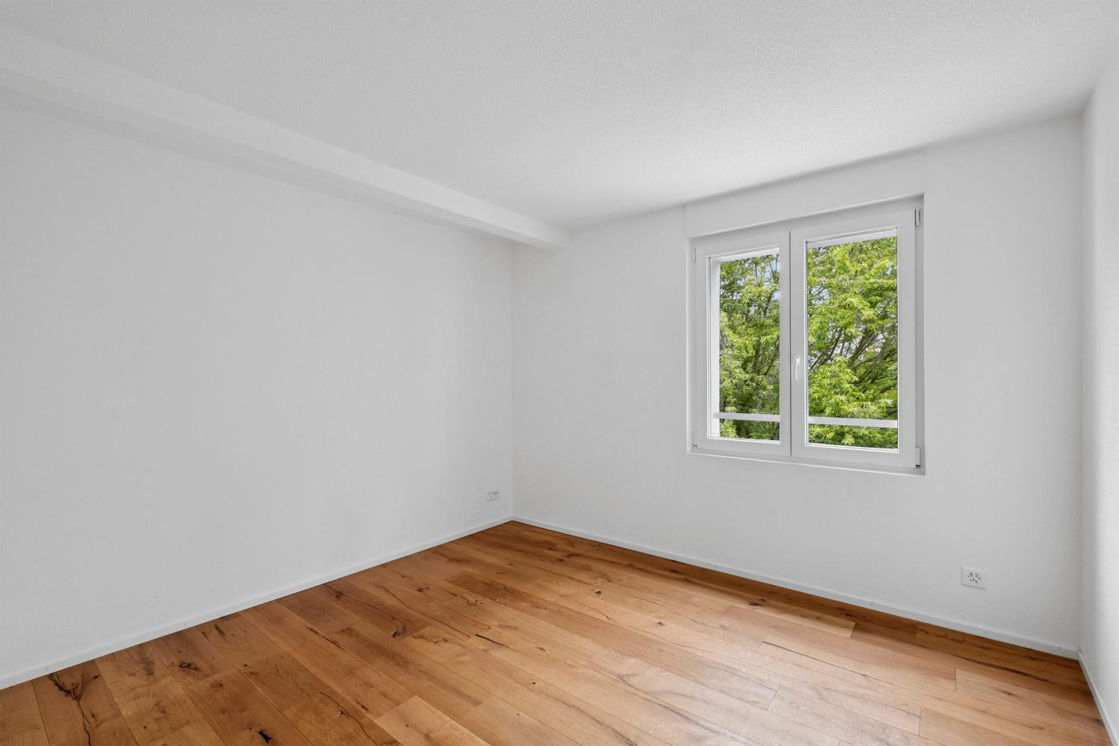Heller leerer Raum mit Holzfußboden und Fensterblick ins Grüne
