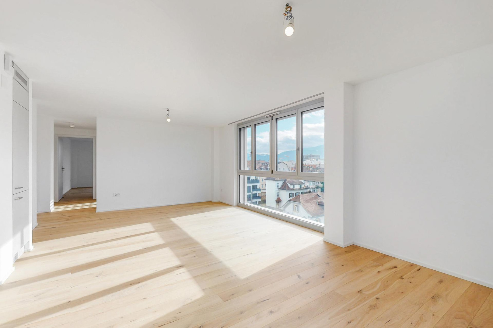 Heller leerer Wohnraum mit großem Fenster und Holzfußboden