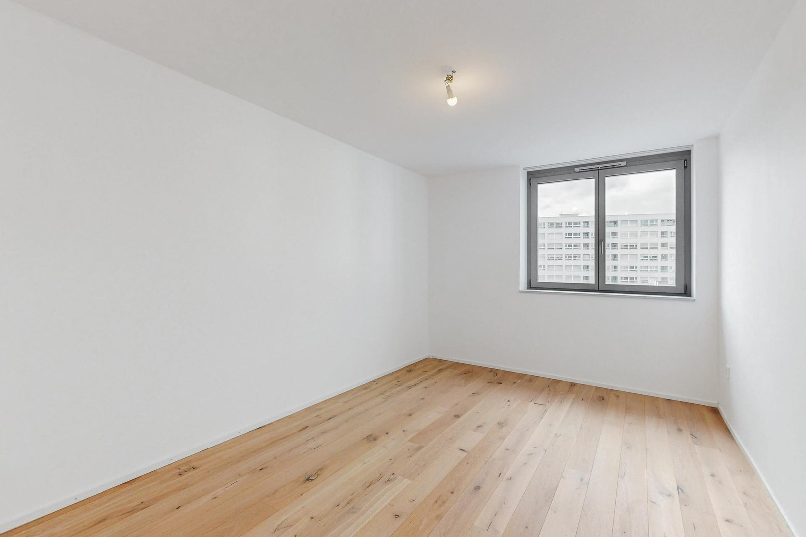 Helles, leeres Zimmer mit Holzboden und Fenster