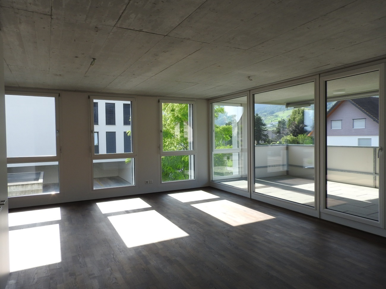 Heller, leerer Wohnraum mit großen Fensterfronten und Balkon