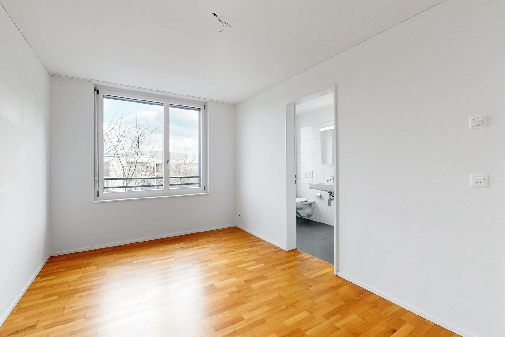 Heller leerer Raum mit Parkettboden und Blick ins Bad