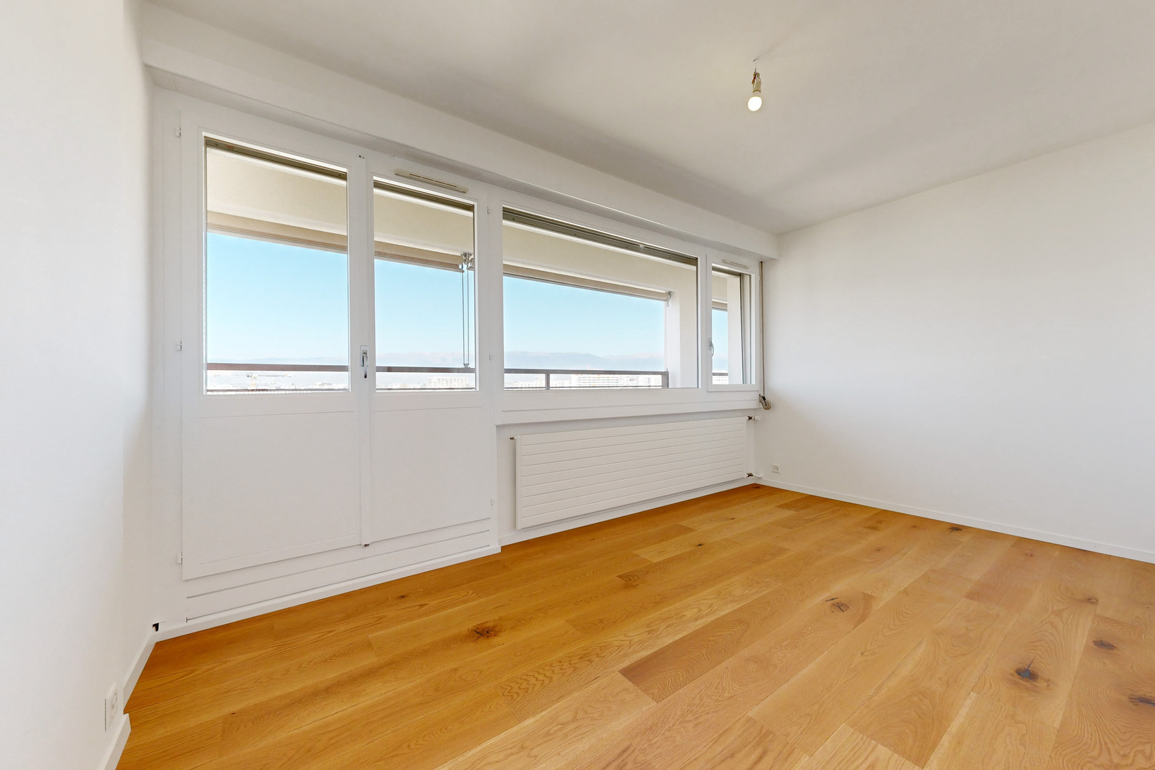 Helles, leeres Zimmer mit großem Fensterfront und Holzparkett