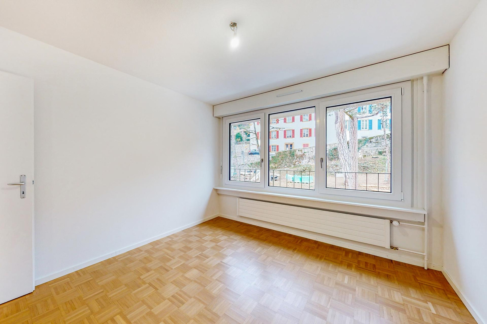 Helles, leeres Zimmer mit Parkett und großem Fenster