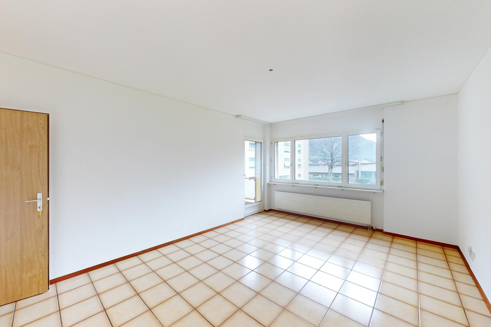 Heller leerer Wohnraum mit Fliesenboden und Fensterfront