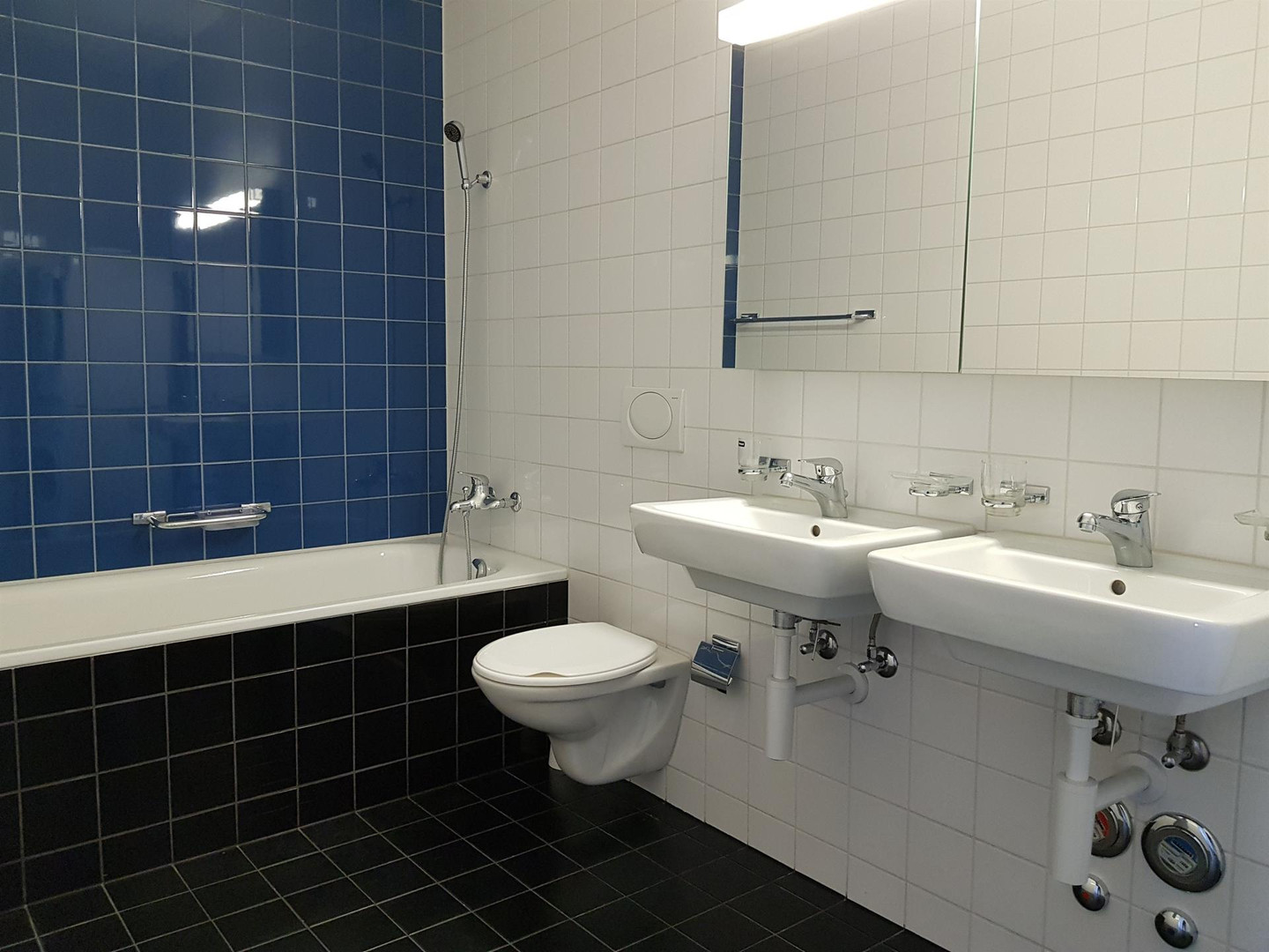 Badezimmer mit Badewanne, Doppelwaschbecken und blau-weißer Kachelgestaltung