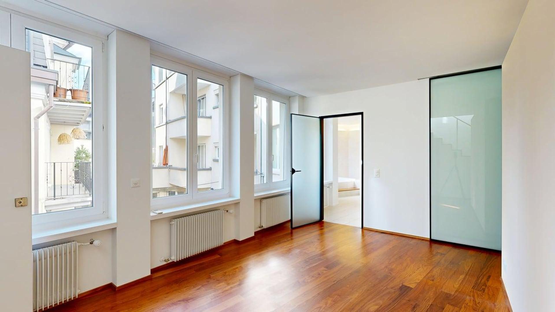 Helles, leerstehendes Zimmer mit großen Fenstern und Holzparkett