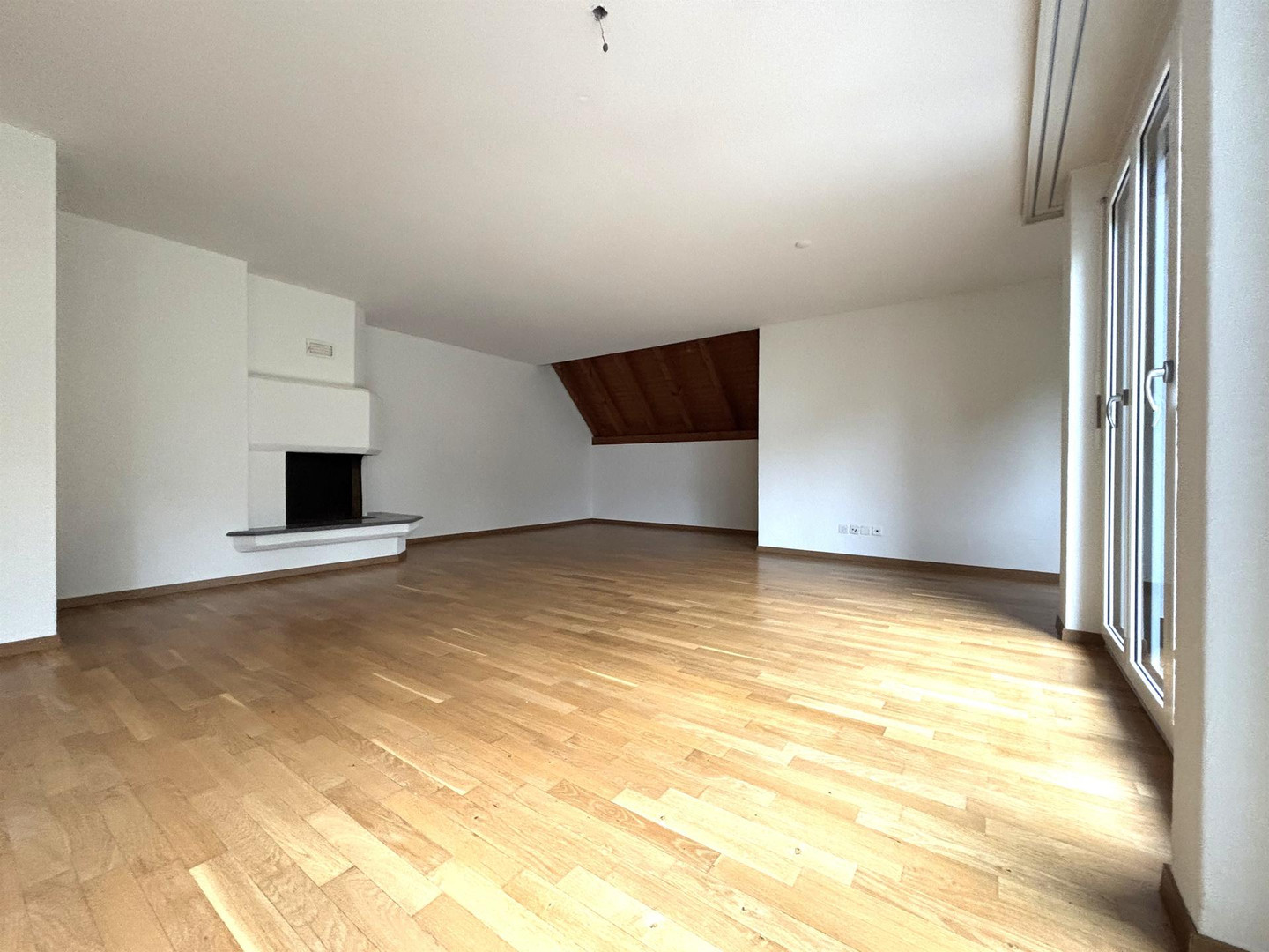 Großer leerer Wohnraum mit Holzparkett, Kamin und Dachschräge