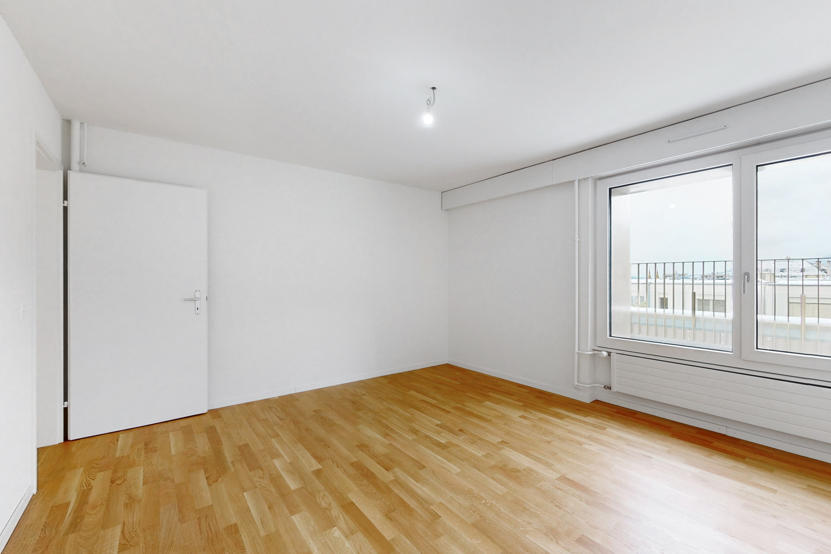 Leerer heller Raum mit Parkett und Balkonfenster