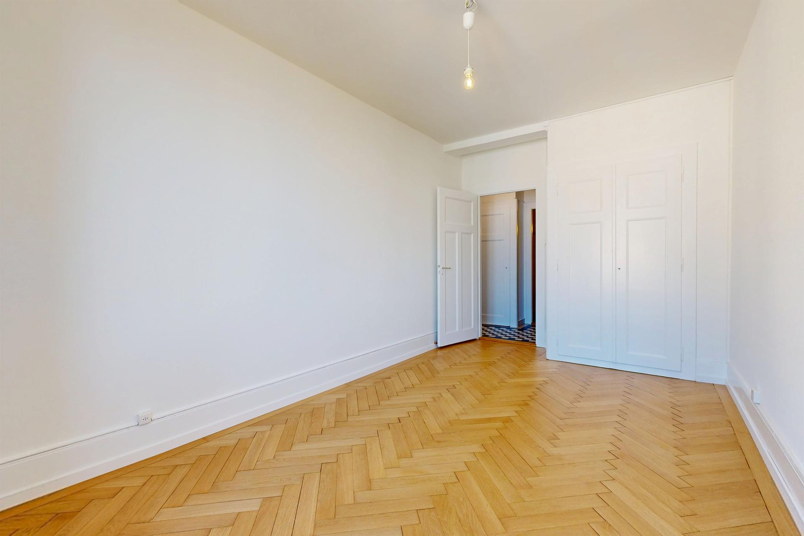 Heller leerer Raum mit Fischgrätparkett und Einbauschrank