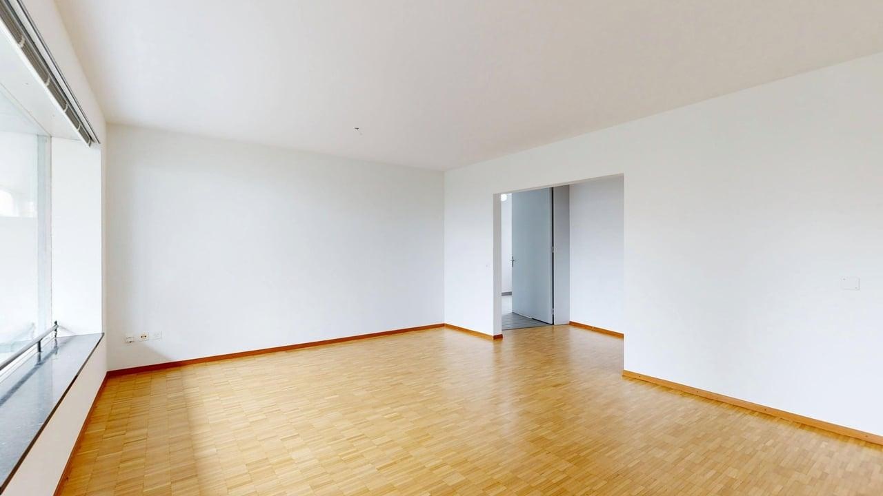 Heller leerer Wohnraum mit Parkettboden und großer Fensterfront