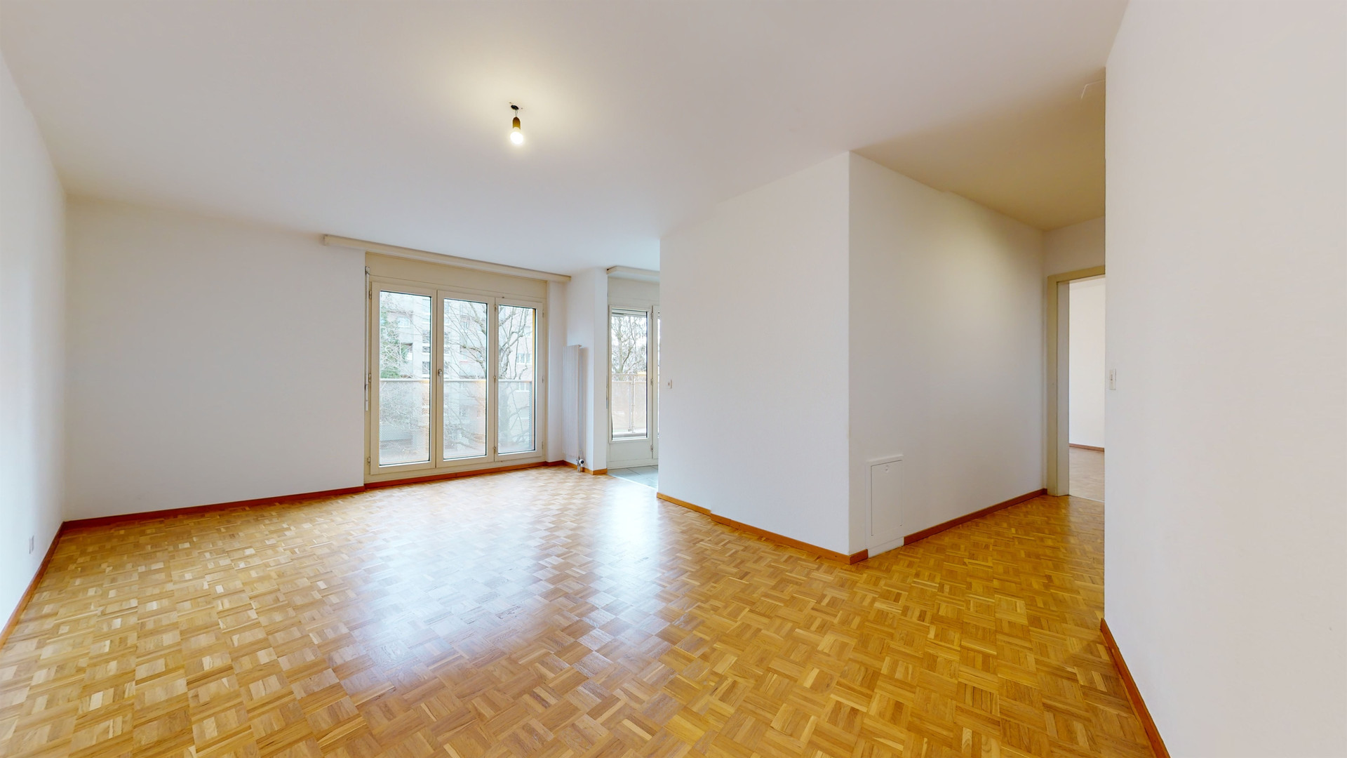 Heller leerer Wohnraum mit Parkettboden und großen Fenstern