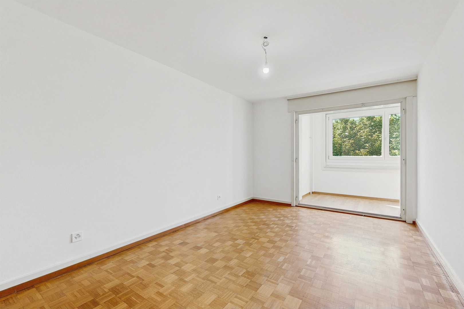 Heller, leerer Raum mit Parkett und Balkonzugang