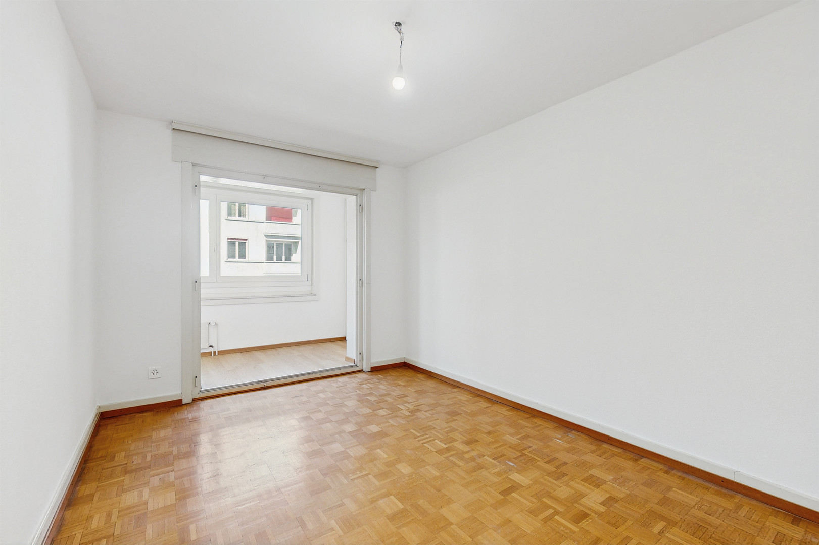 Heller leerer Raum mit Parkettboden und Fenster zum angrenzenden Bereich