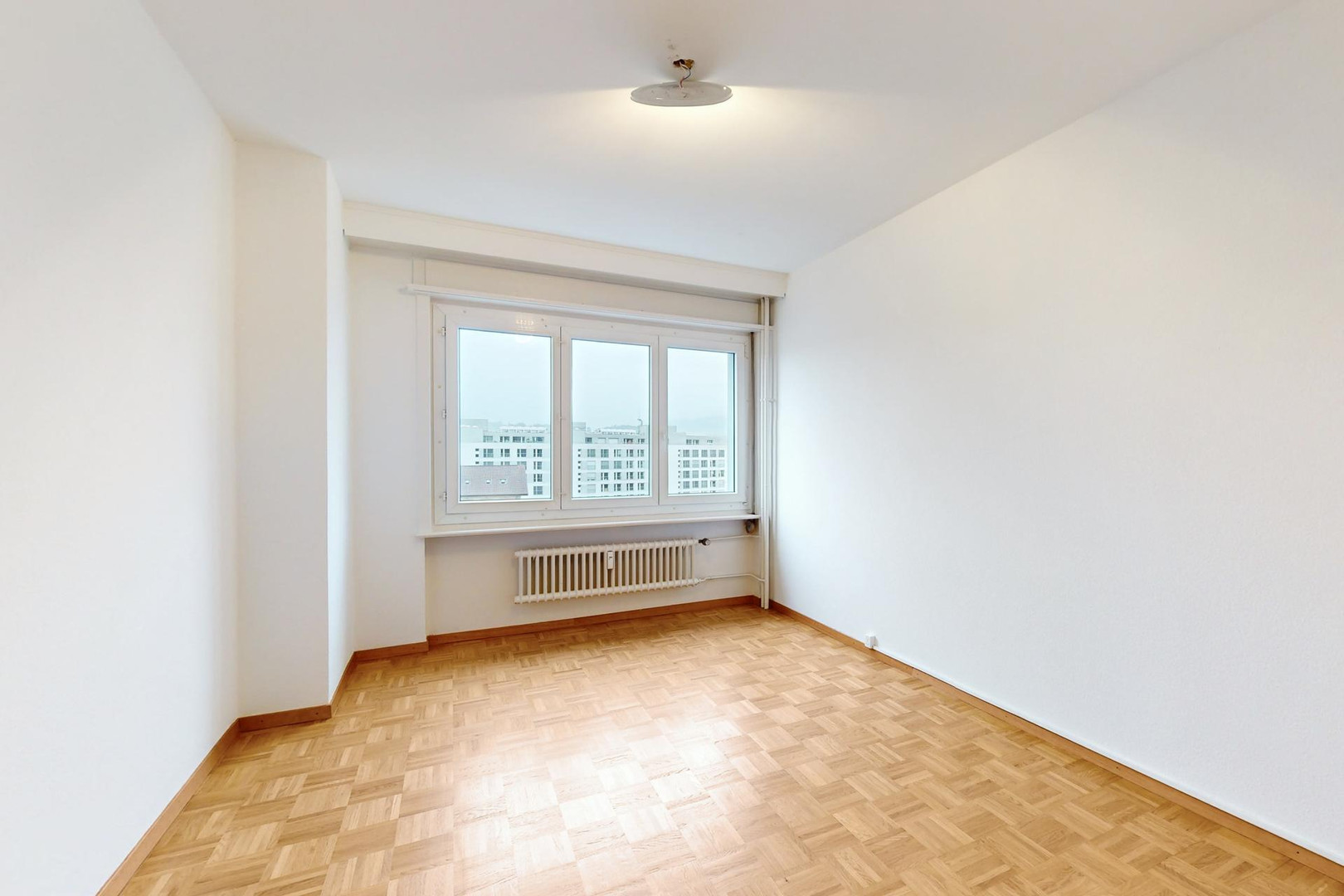 Helles, leeres Zimmer mit Parkettboden und Fensterfront