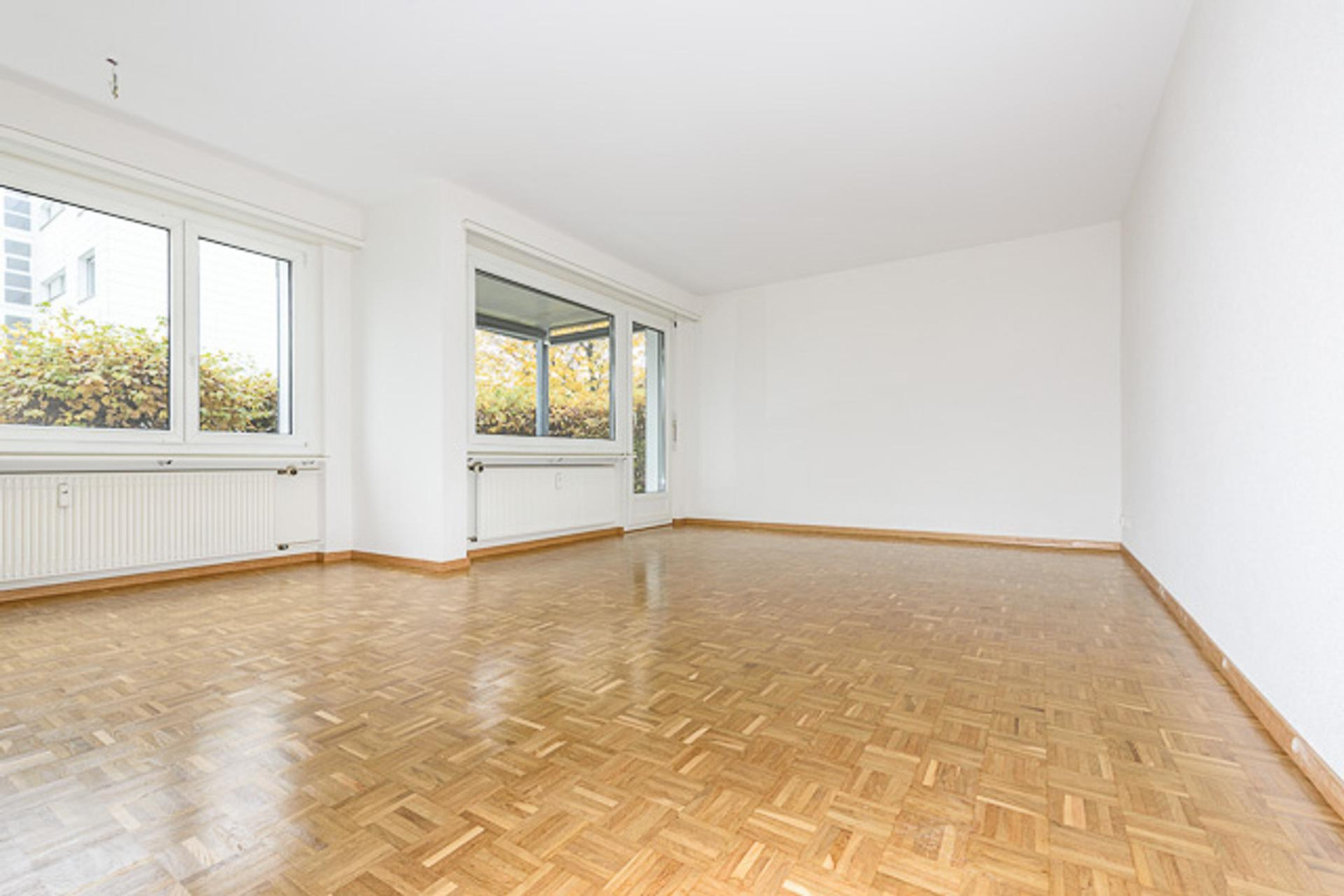 Heller leerer Wohnraum mit Parkettboden und großen Fenstern