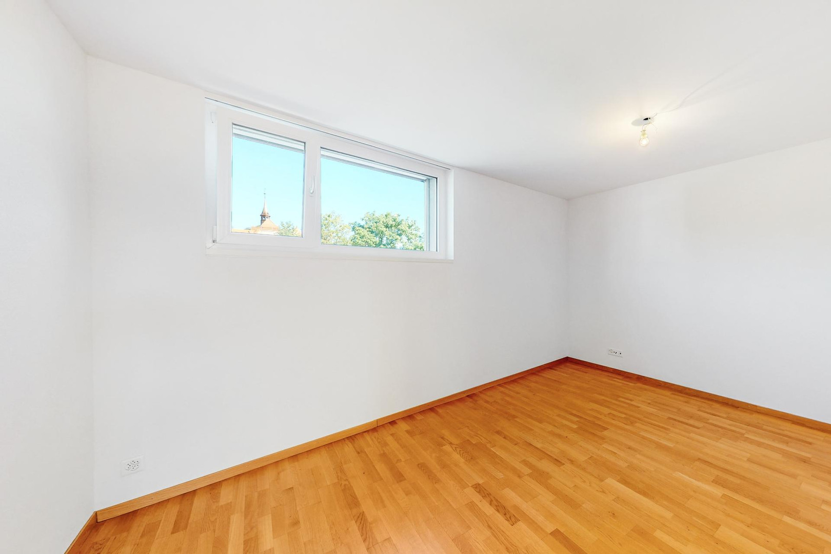 Helles, leeres Zimmer mit Parkettboden und Fenster