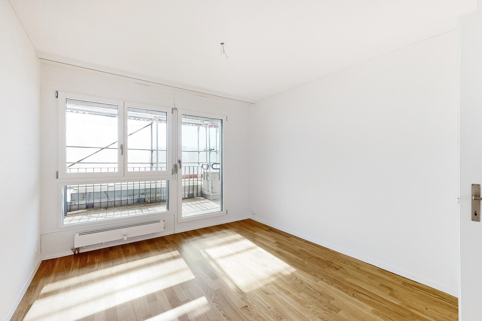 Helles leeres Zimmer mit Holzboden und Balkonfenster