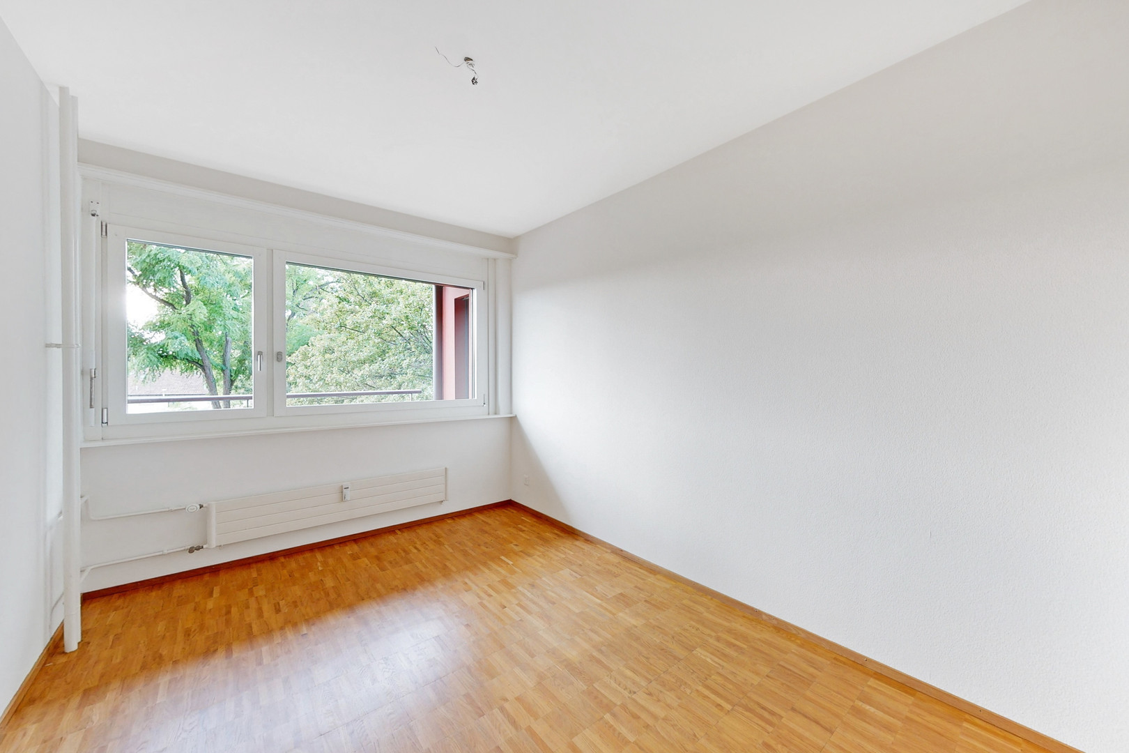 Helles, leeres Zimmer mit Parkettboden und großem Fenster