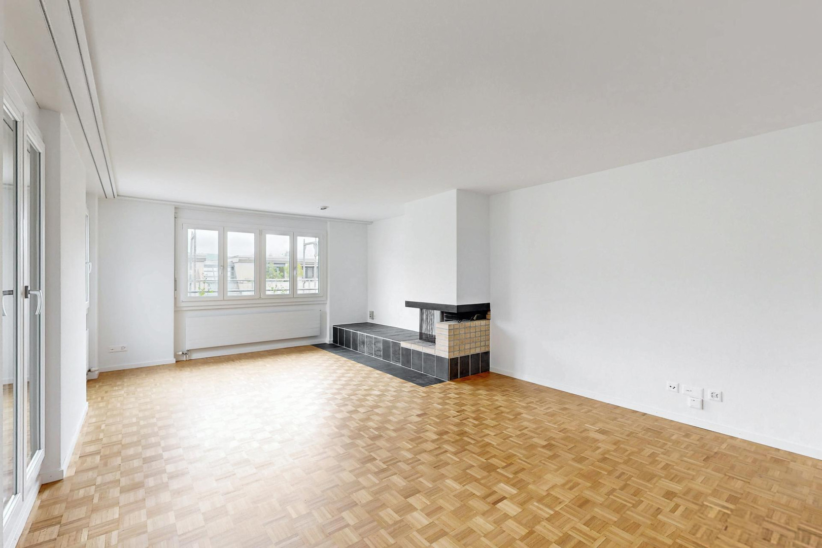 Heller leerer Wohnraum mit Kamin und Parkettboden