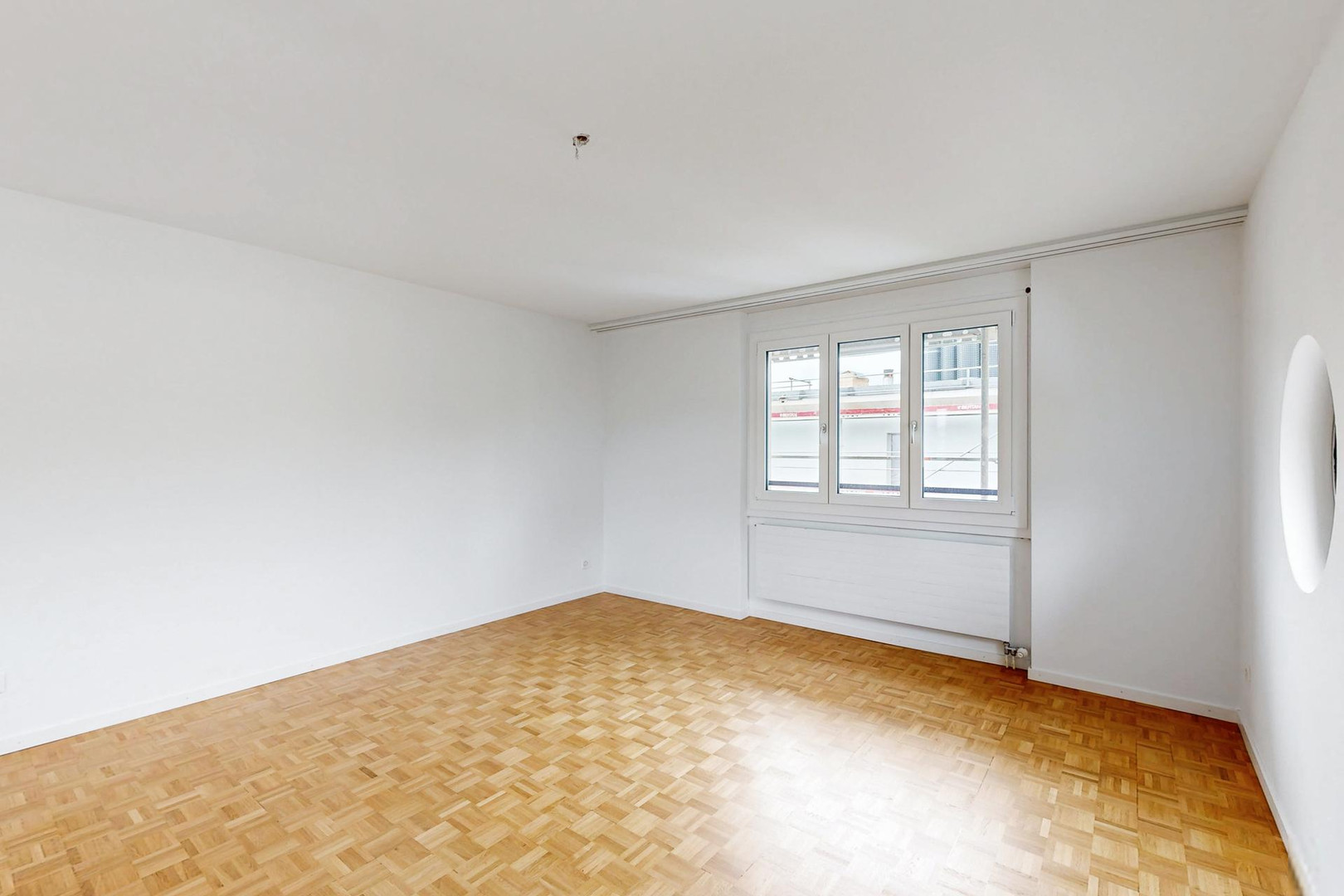Leerer heller Raum mit Parkettboden und Fenster