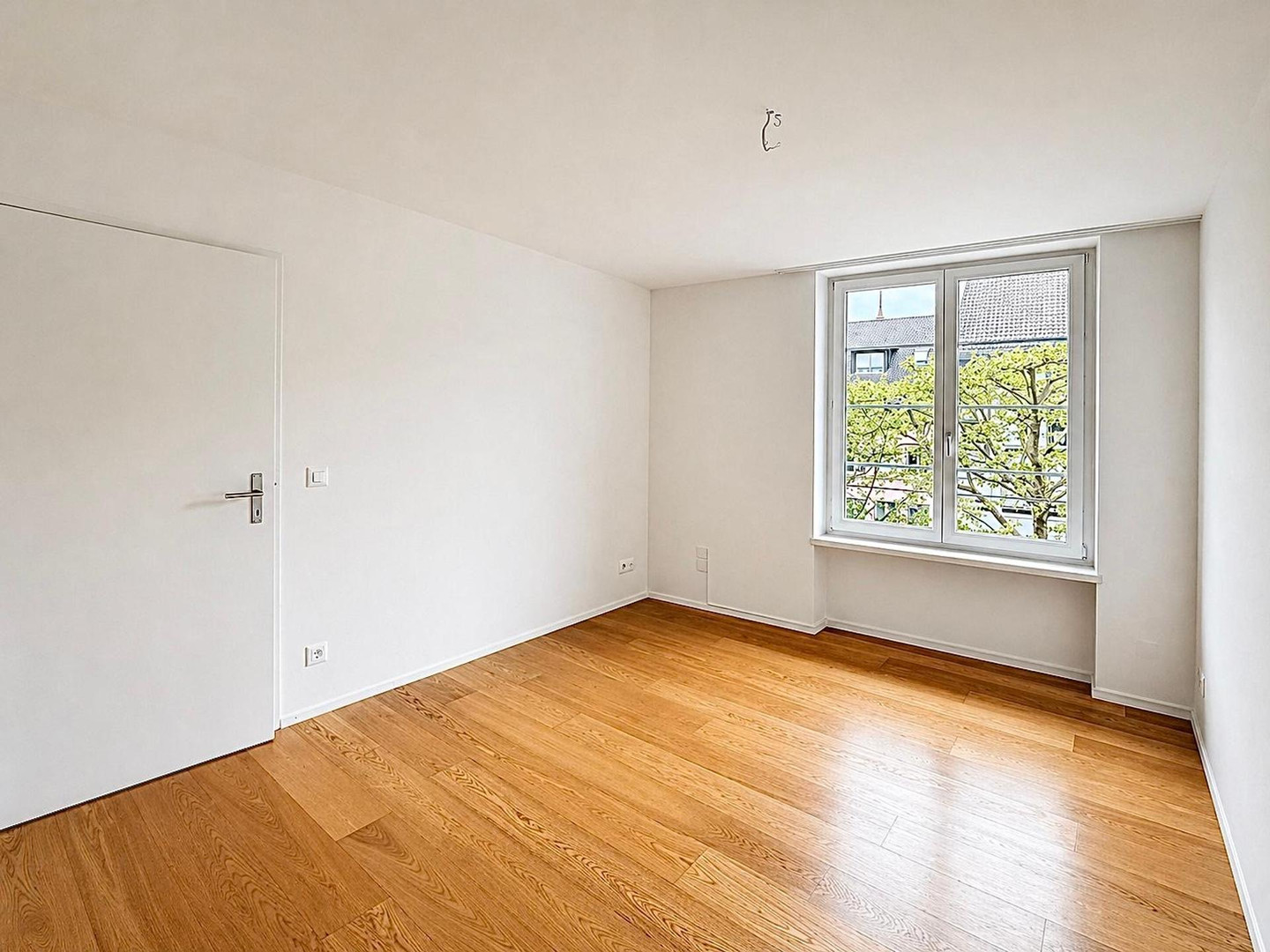 Helles, leeres Zimmer mit Holzboden und Fensterblick