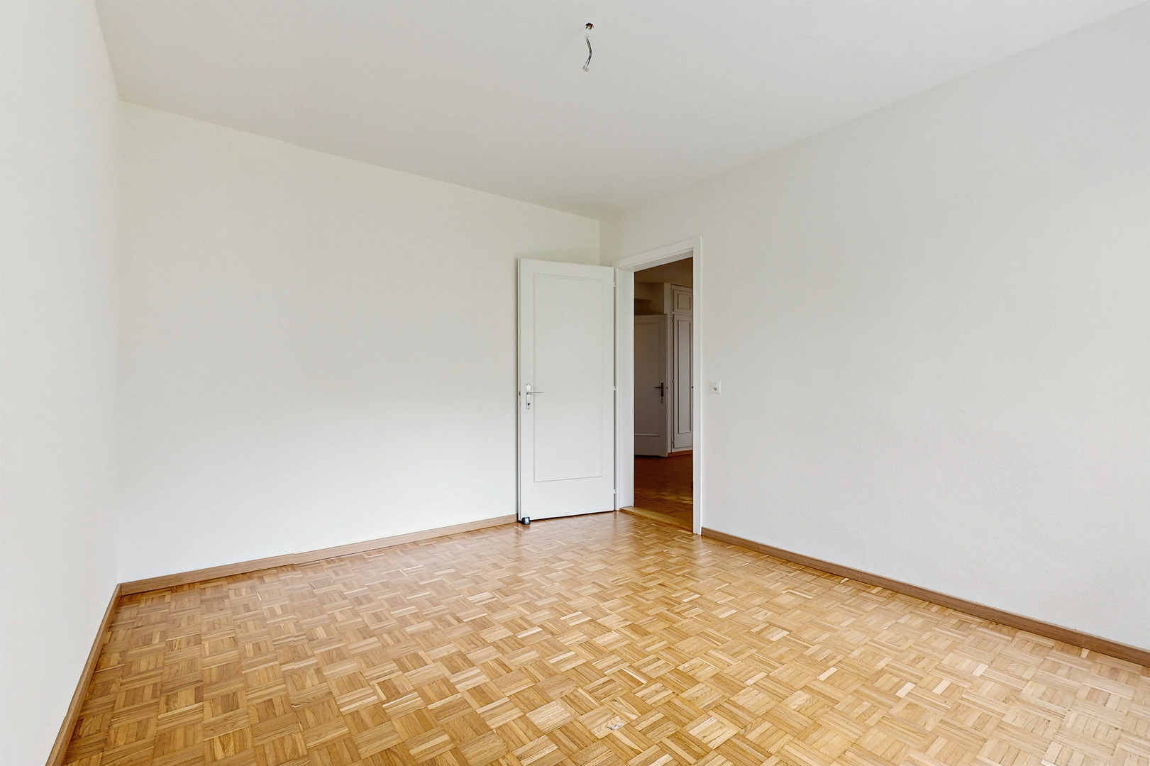 Leerer Wohnraum mit Parkettboden und offener Tür