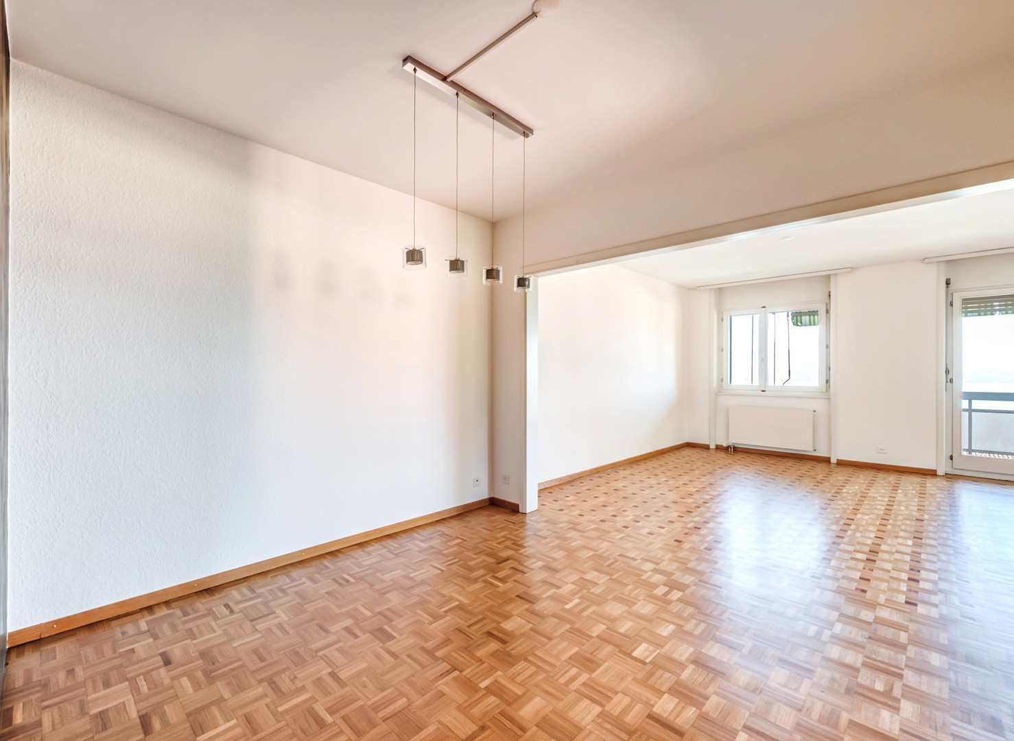 Heller leerer Wohnraum mit Parkettboden und Durchgang zum Nebenraum