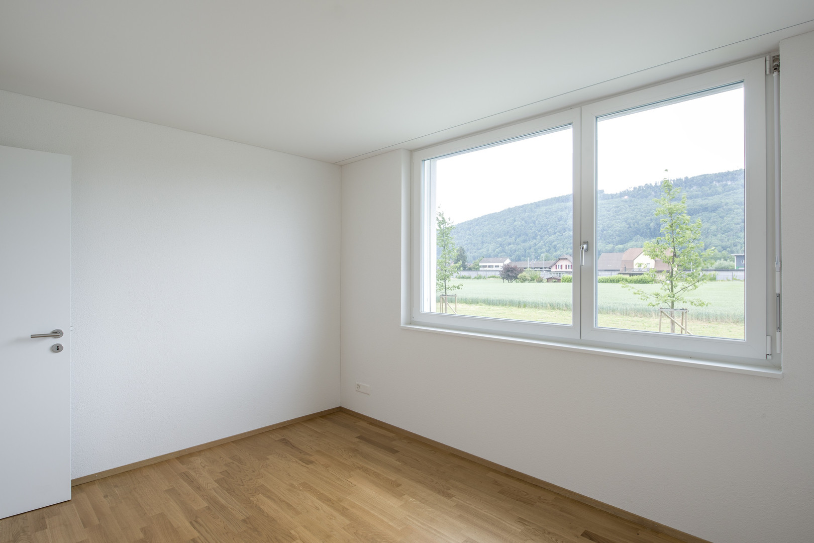 Helles leeres Zimmer mit großem Fenster und Holzfußboden