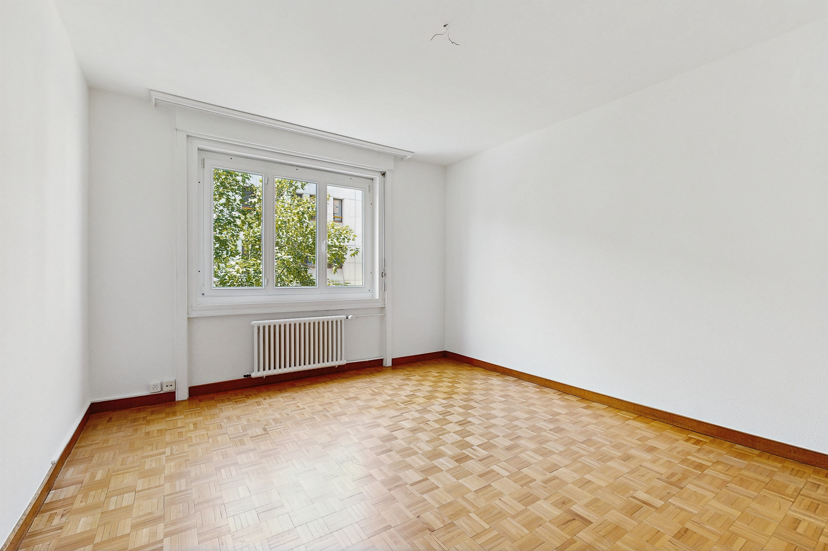 Leerer heller Raum mit Parkettboden und Fenster