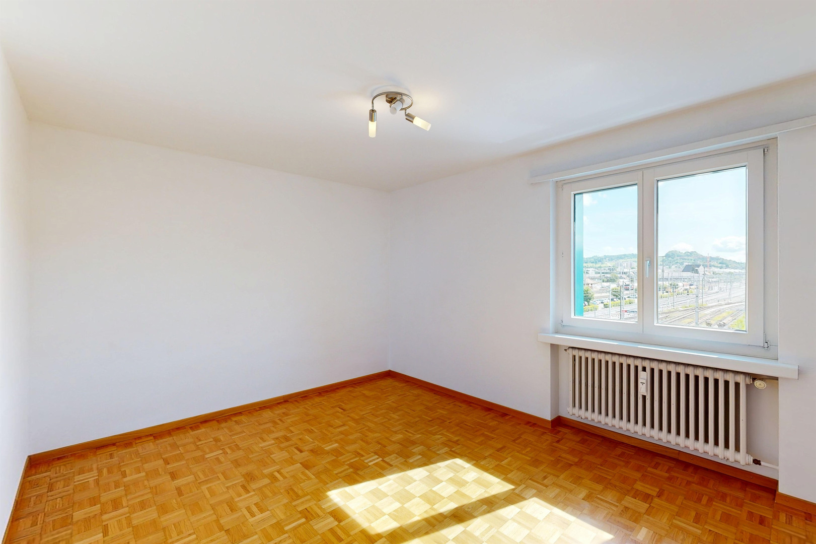 Heller leerer Raum mit Parkettboden und Fensterblick