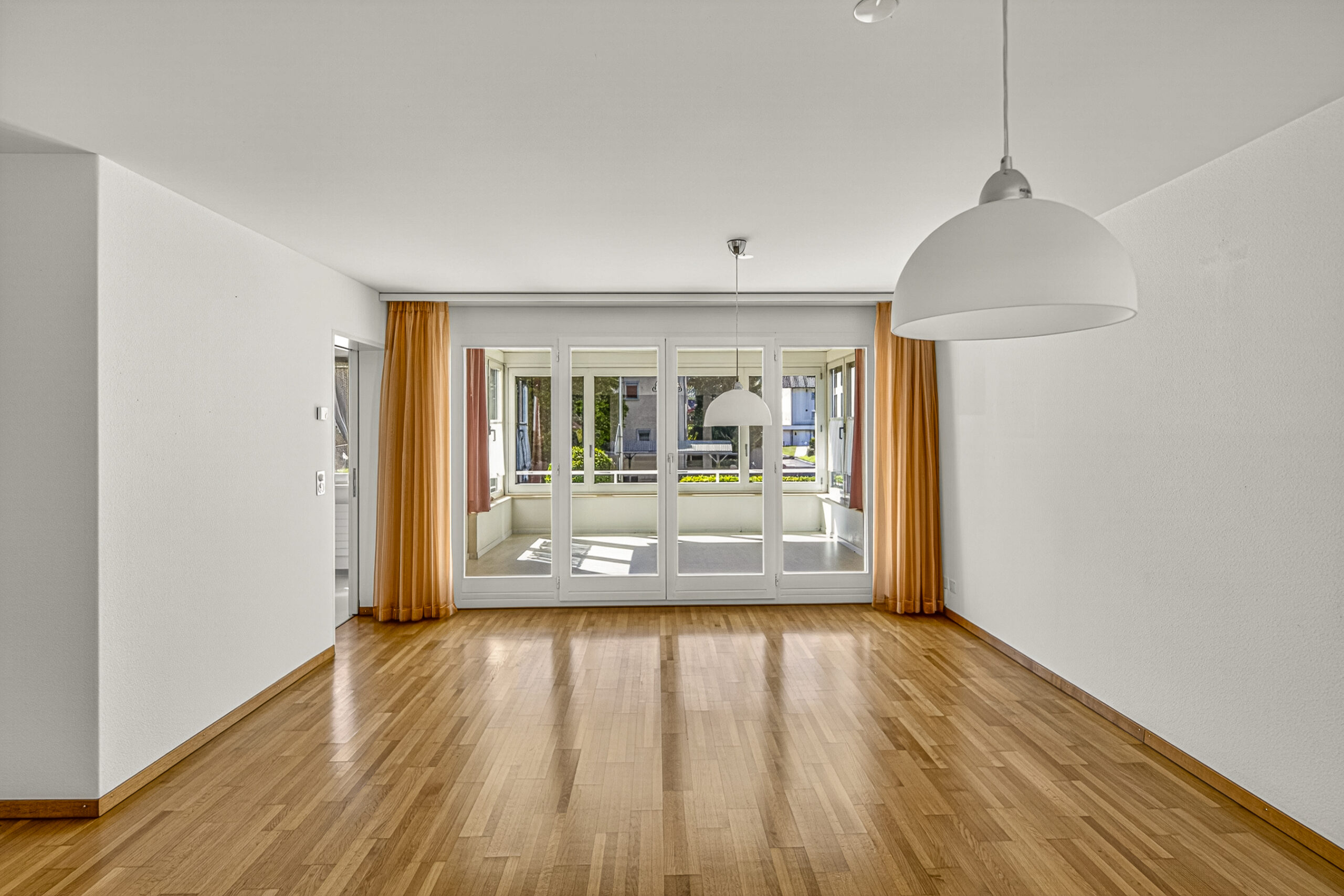 Heller leerer Wohnraum mit Holzparkett und großer Fensterfront