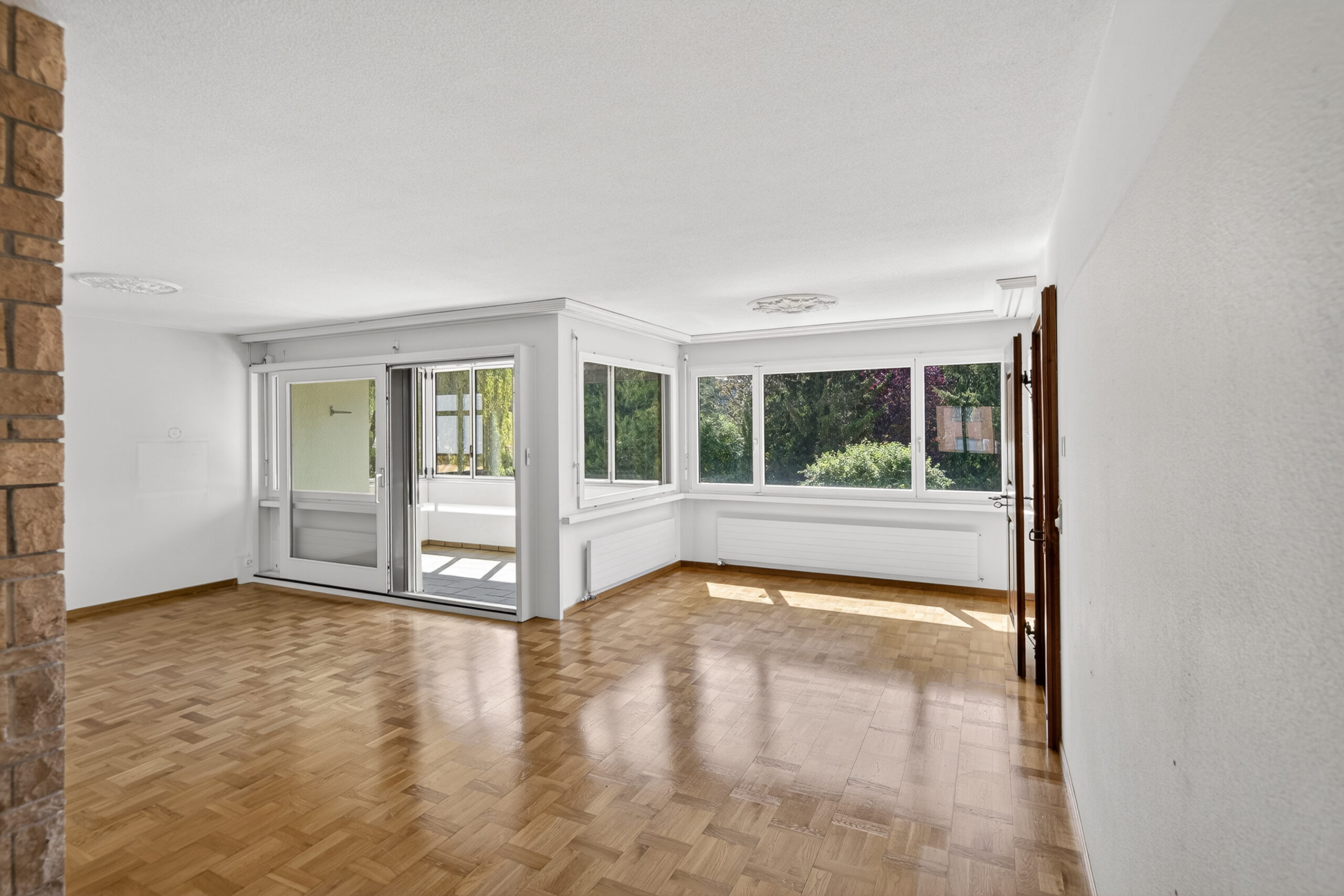 Heller leerer Wohnraum mit Parkettboden und großen Fenstern