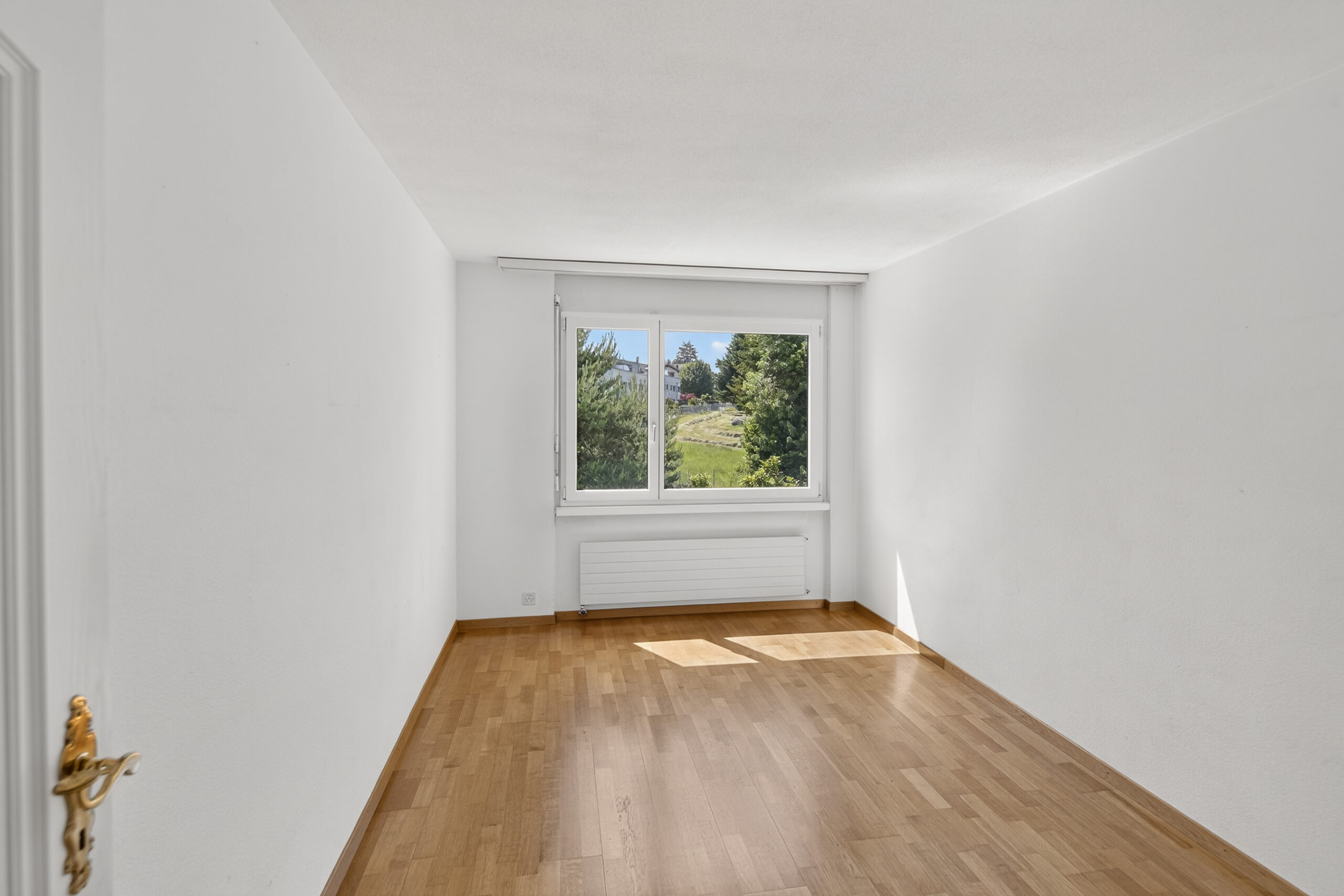 Helles, leeres Zimmer mit Fenster und Holzfußboden