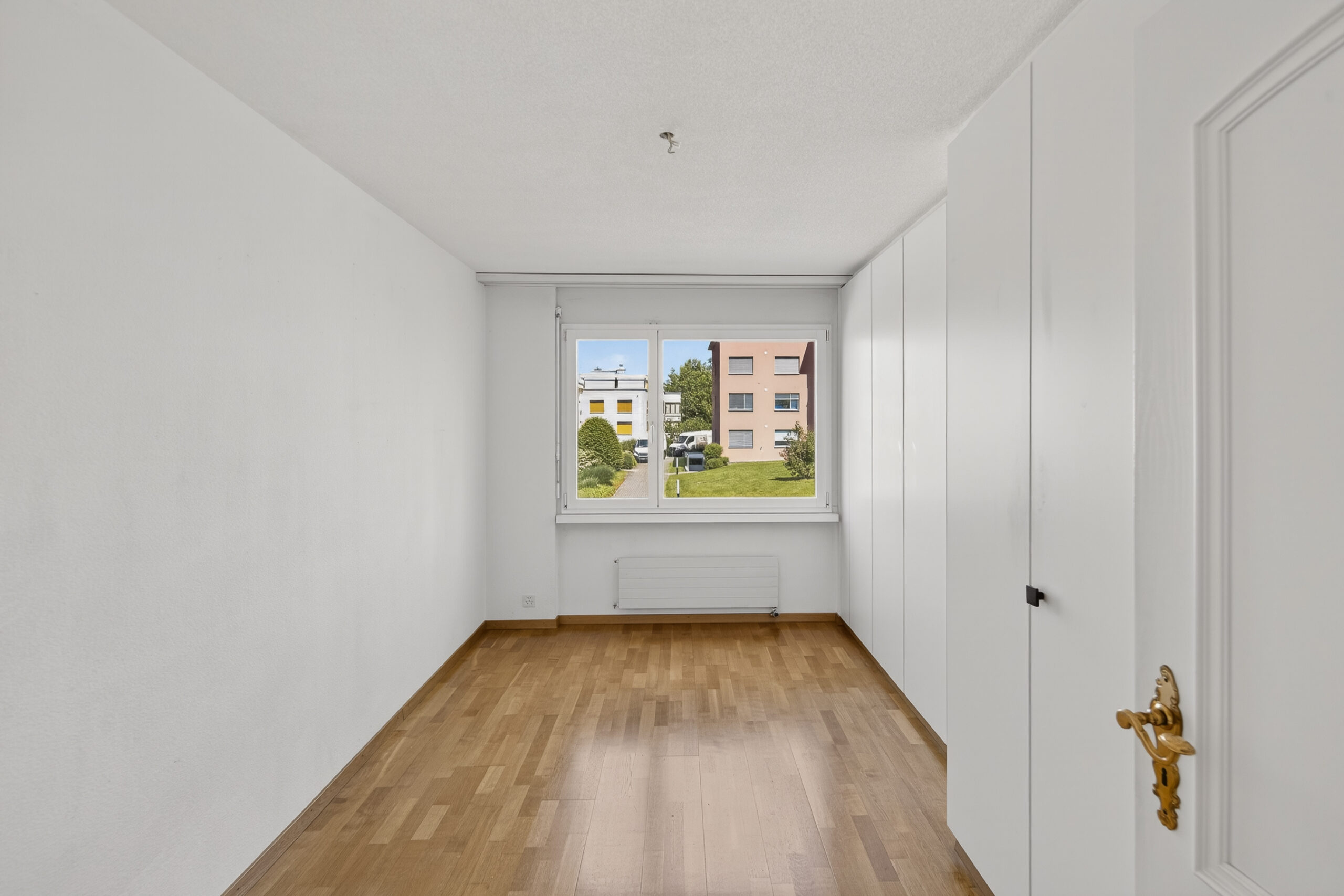 Helles, leeres Zimmer mit Fensterfront und Einbauschrank