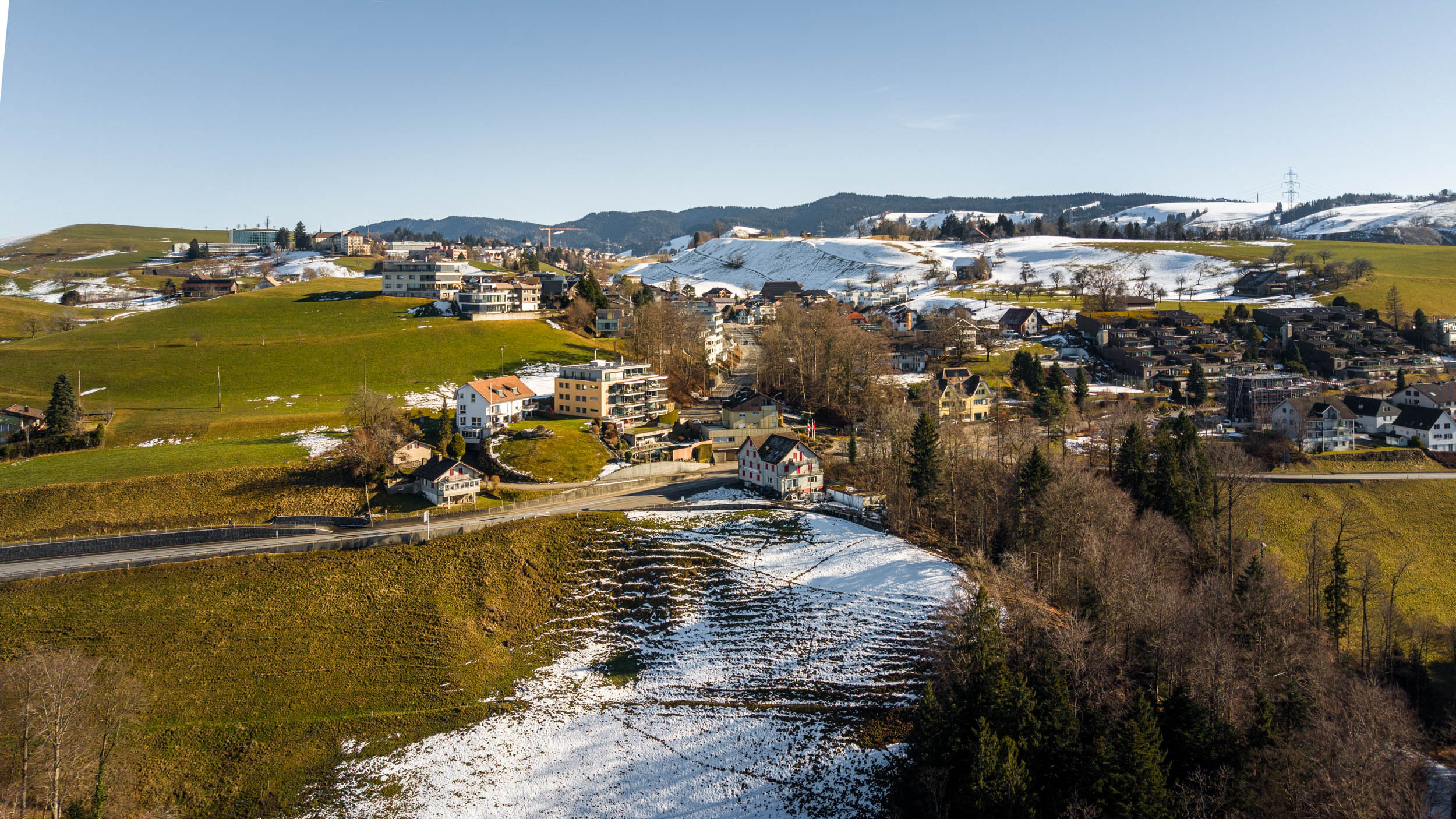 Landschaftsaufnahme eines ländlichen Ortes mit Hügeln und Schneefeldern