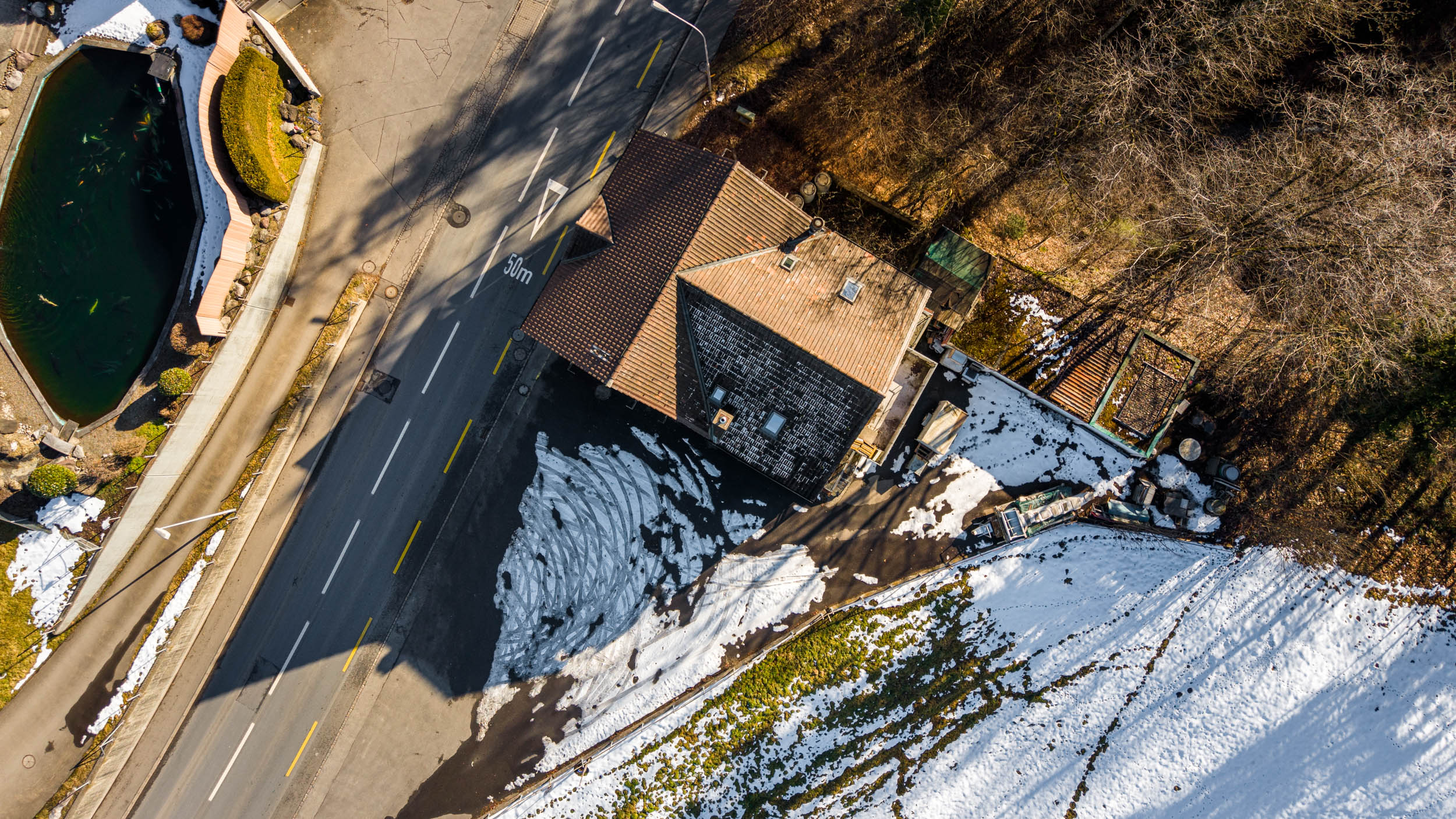 Luftaufnahme eines Hauses an einer Straße neben einem Teich und Waldflächen