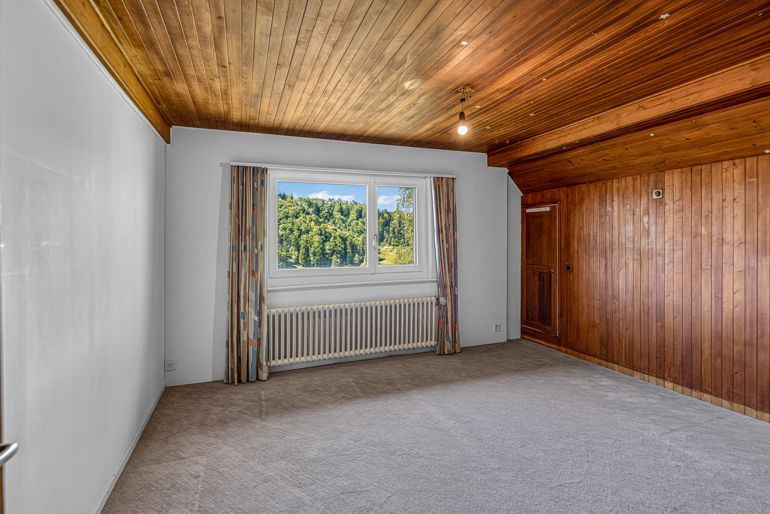 Leerer Dachraum mit Holzdecke und Ausblick ins Grüne