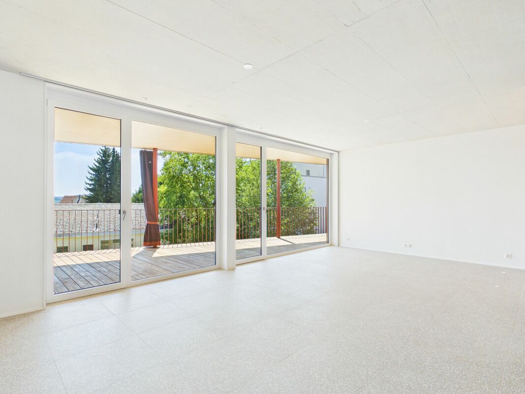 Heller leerer Wohnraum mit großer Fensterfront und Terrasse