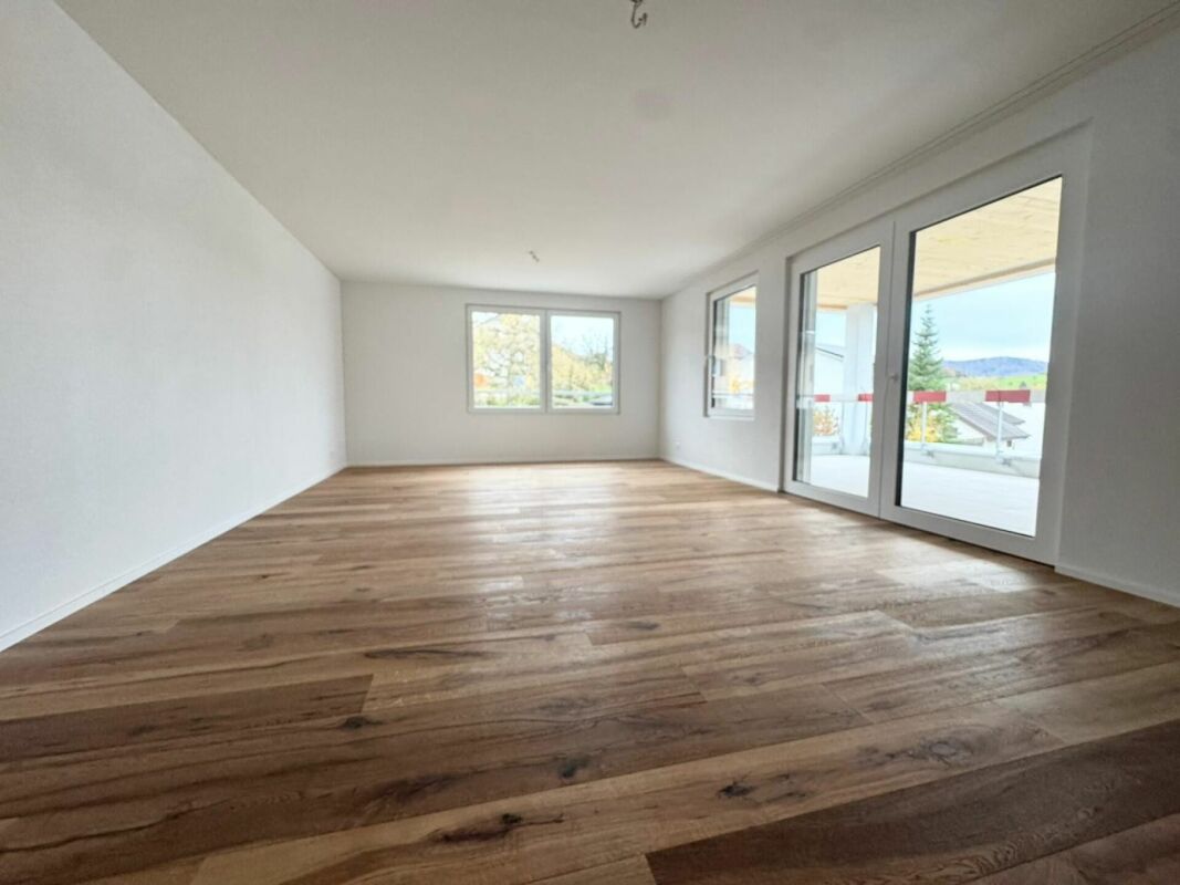 Leerer heller Wohnraum mit Holzoptik-Boden und Balkonzugang