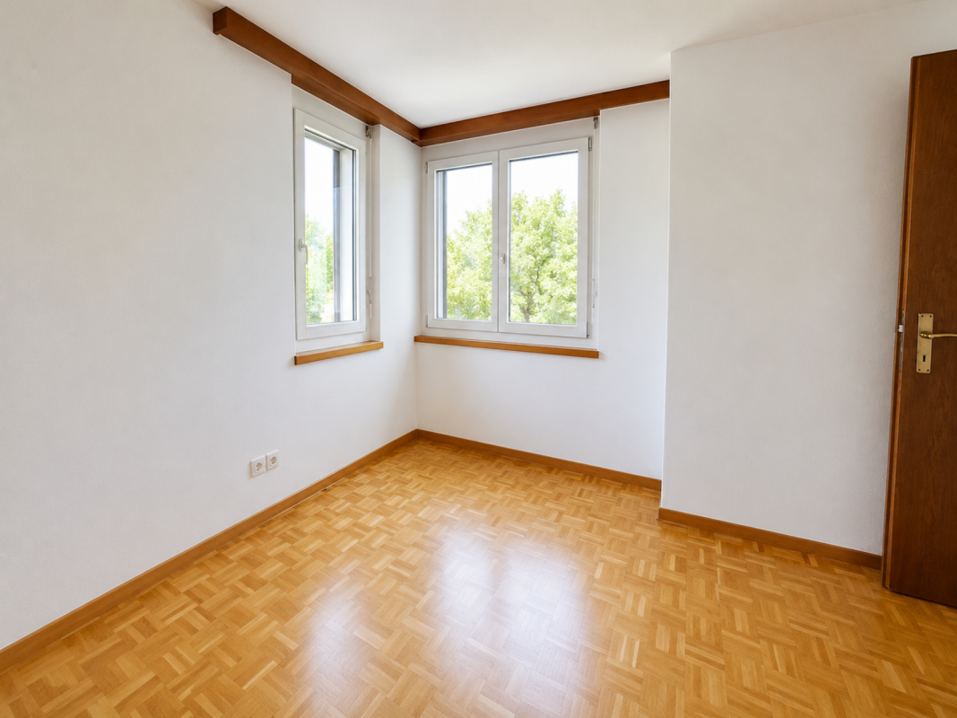 Heller leerer Raum mit Parkettboden und zwei Fenstern