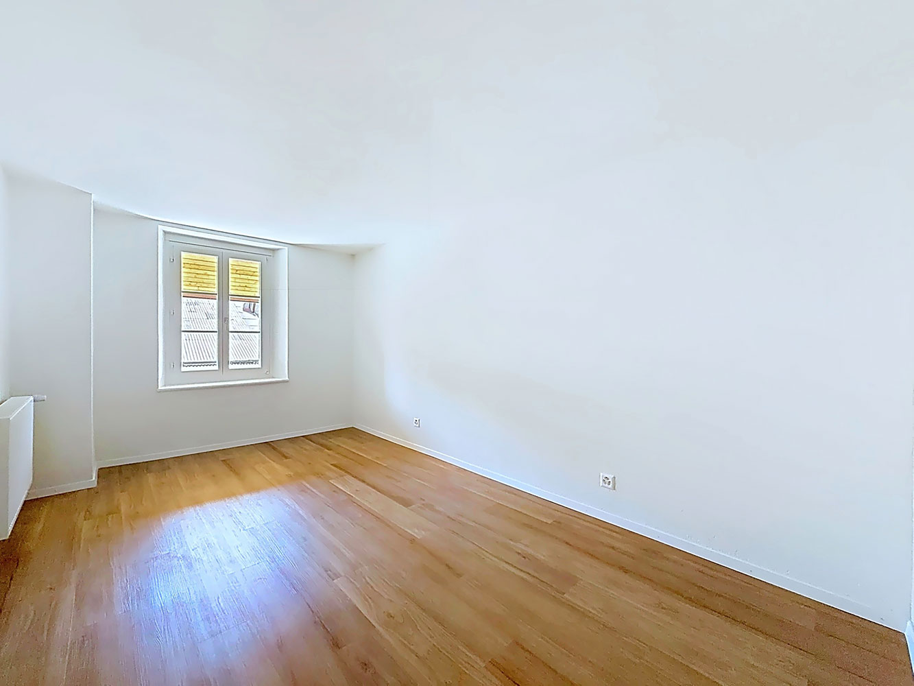 Helles, leeres Zimmer mit Holzfußboden und kleinem Fenster