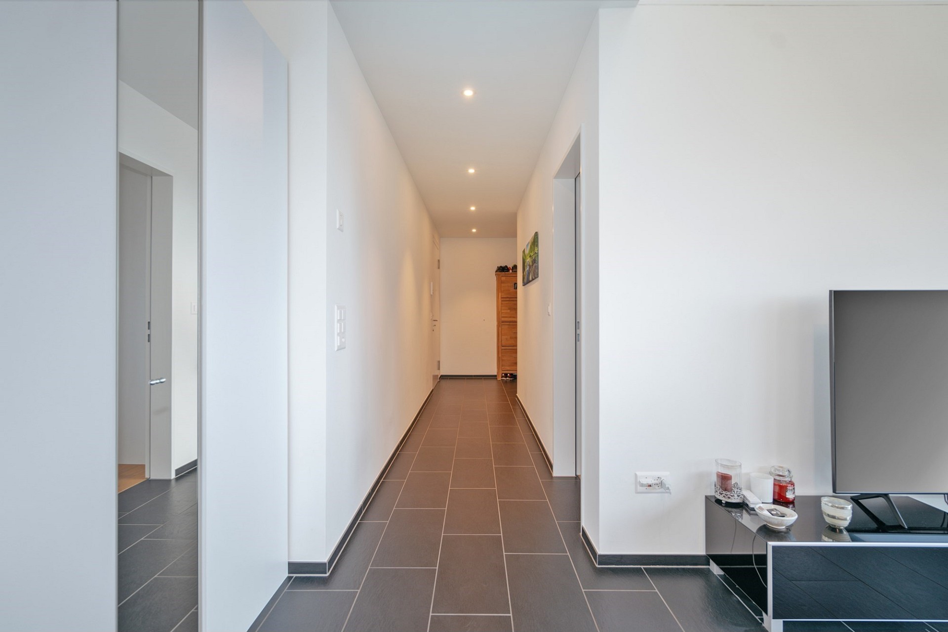 Langer, moderner Flur mit hellen Wänden und dunklem Fliesenboden